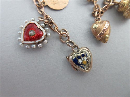 Lot 335 - A charm bracelet with two antique enamelled heart lockets and a half sovereign amongst other charms
