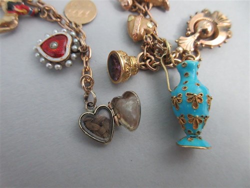 Lot 335 - A charm bracelet with two antique enamelled heart lockets and a half sovereign amongst other charms