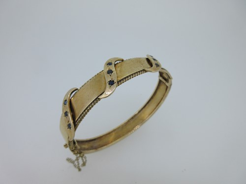Lot 83 - A hinged gold bangle set with sapphires