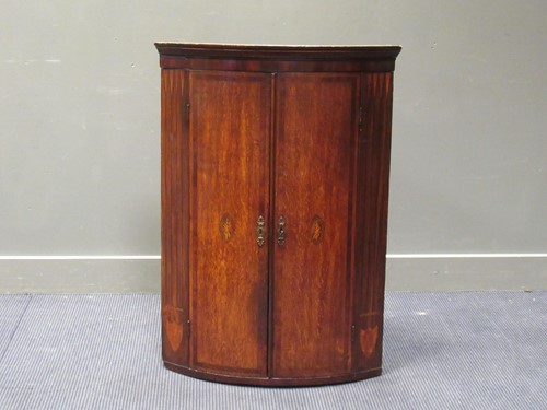Lot 555 - A George III inlaid oak two door bow front...