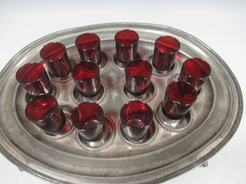 Lot 11 - A pewter shot holder tray with twelve red glasses
