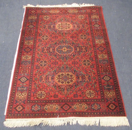 Lot 852 - A red ground woollen rug decorated with three...